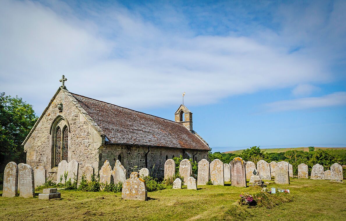 A stone church with a cross on top, surrounded by a graveyard with headstones.