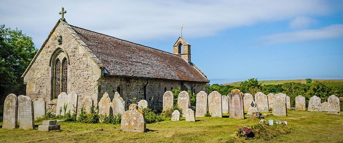A stone church with a cross on top, surrounded by a graveyard with headstones.