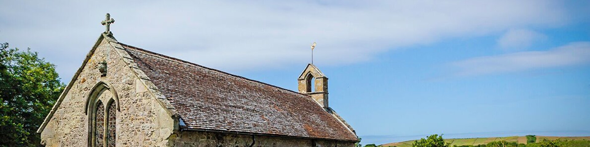 A stone church with a cross on top, surrounded by a graveyard with headstones.