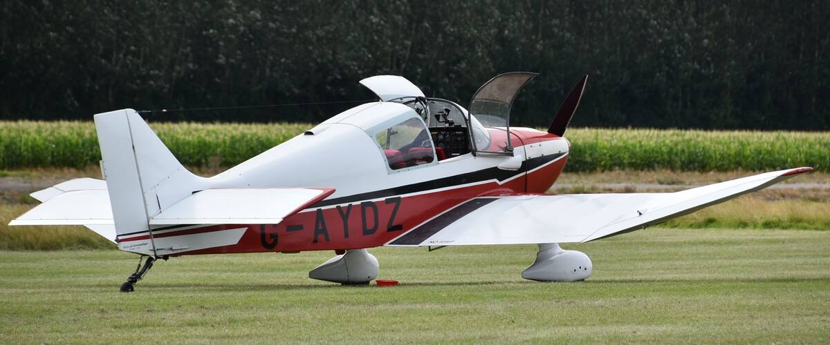 A small white and red aircraft with the registration G-AYDZ parked on a grassy field.