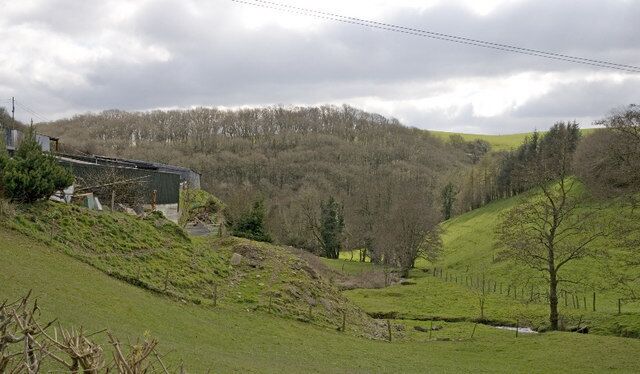 A rural landscape with a house, a hill, and a forest.