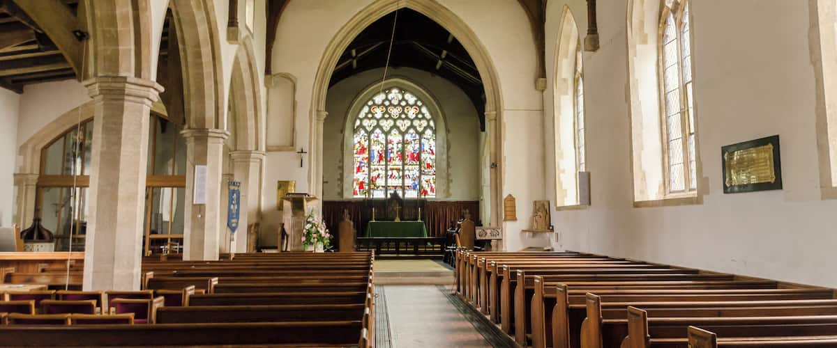 A church interior with wooden pews, stained glass windows, and arched ceilings.