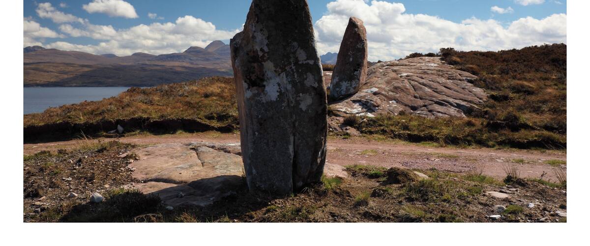 A landscape with two large standing stones and a lake in the background.