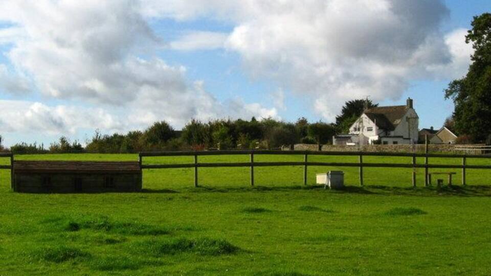 A green field with a wooden fence, a white house, and a barn in the background.