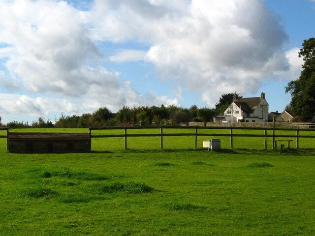 A green field with a wooden fence, a white house, and a barn in the background.
