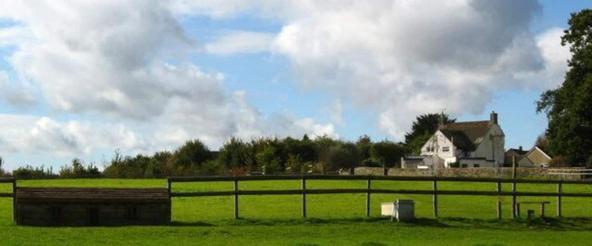 A green field with a wooden fence, a white house, and a barn in the background.