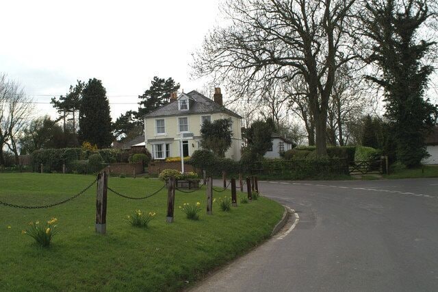 A residential street with a house, a grassy area, and a chain-link fence.