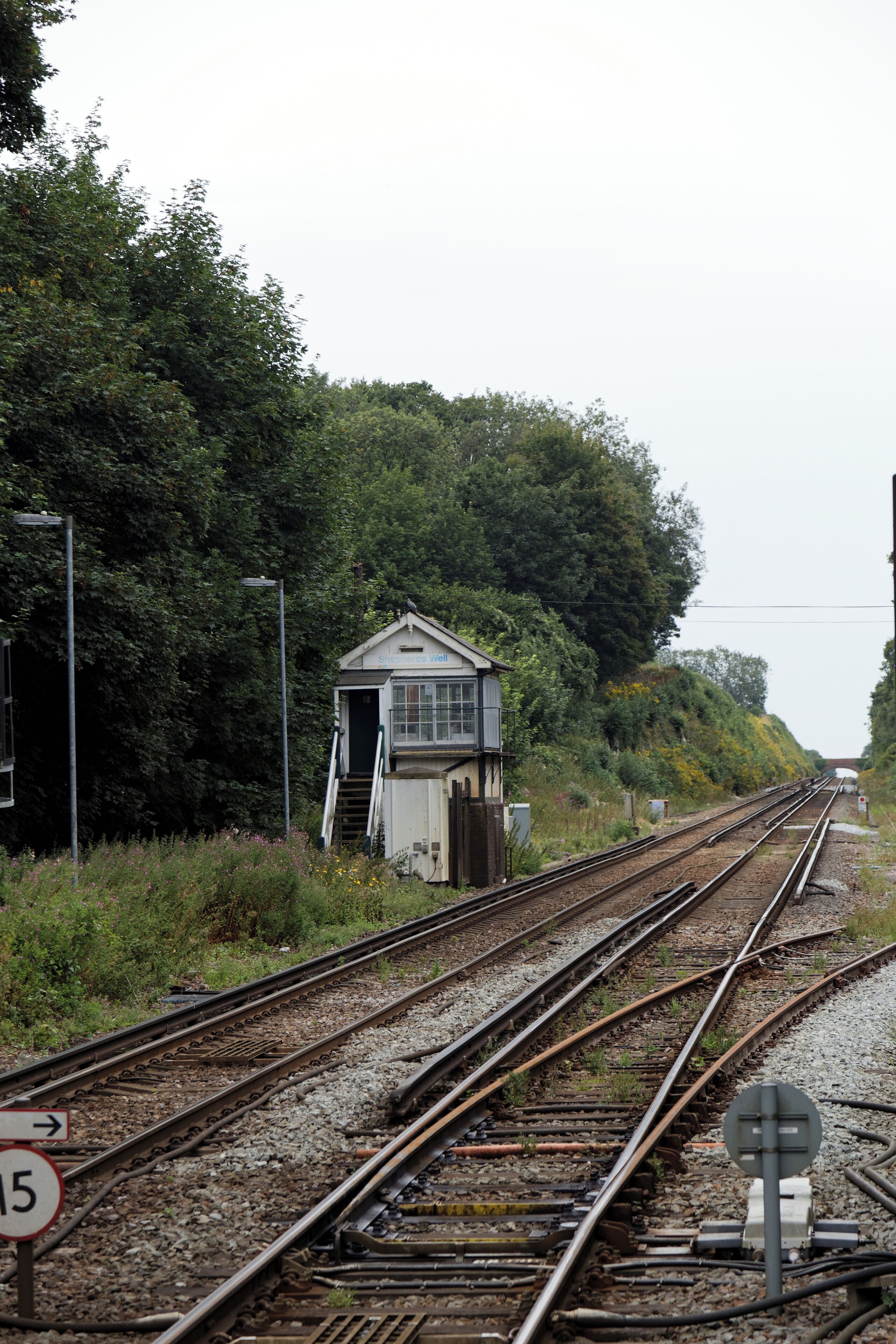 Railway tracks with a small signal box and a speed limit sign.