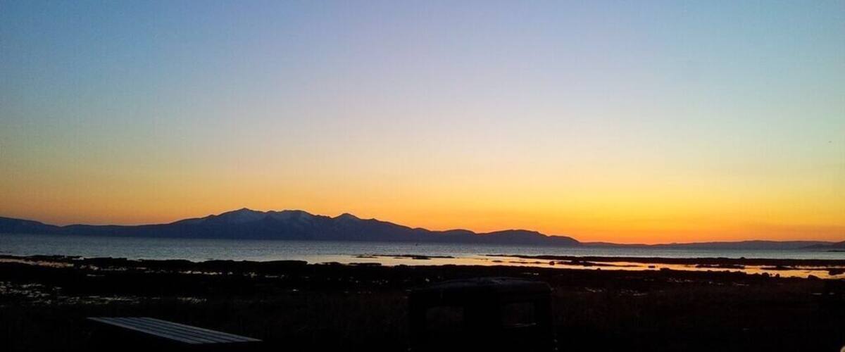 A sunset over a coastal landscape with mountains in the distance.