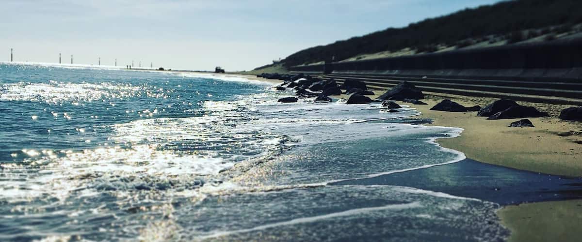 A beach with waves, a sandy shore, and a distant bridge.