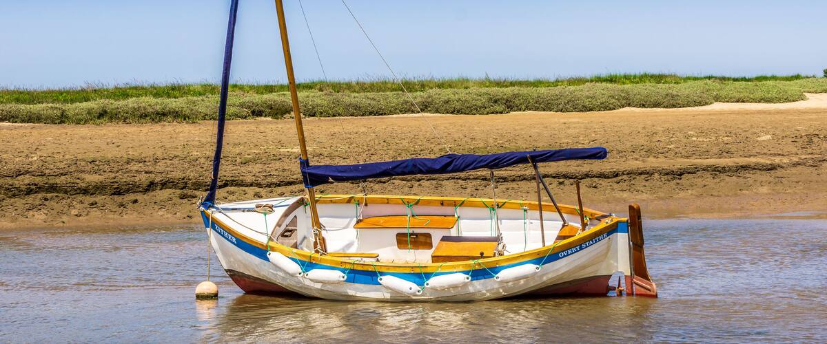 White sail boat beached at low tide, Burnham Overy Staithe, Norfolk