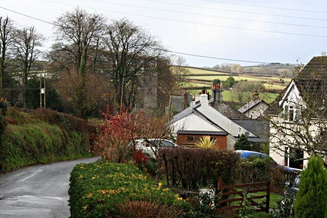 A rural road with houses, a church, and a car parked on the side.