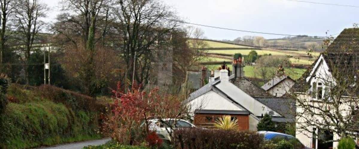 A rural road with houses, a church, and a car parked on the side.