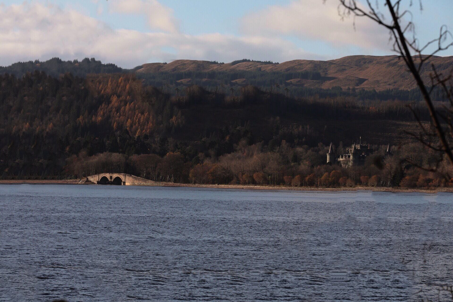 A bridge over a body of water, surrounded by hills and a castle in the distance.
