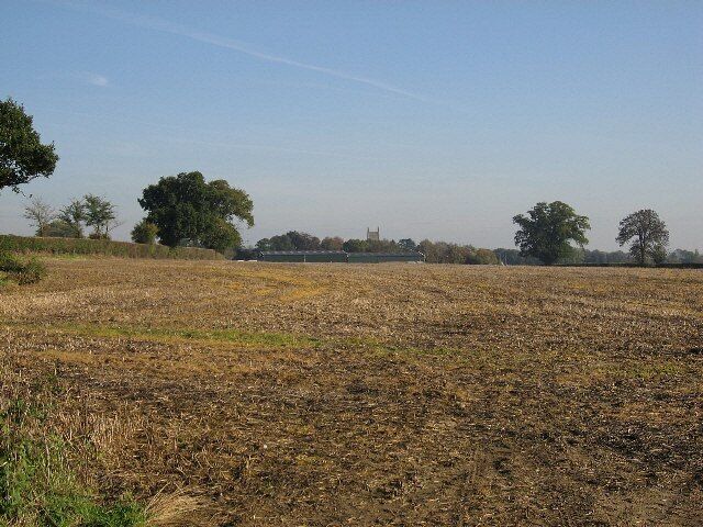 God And Mammon A field stretches to barns and a church in the distance.