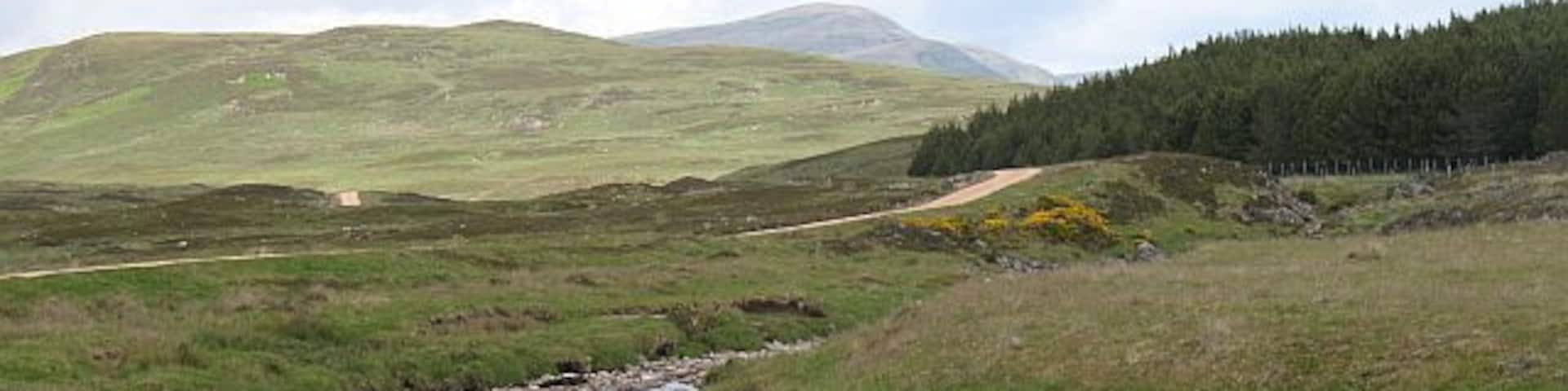 A stream flowing through a grassy valley with hills in the background.