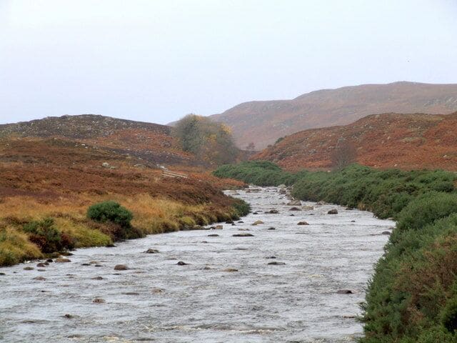 Un río serpentea a través de un paisaje montañoso, con terreno rocoso y vegetación escasa.
