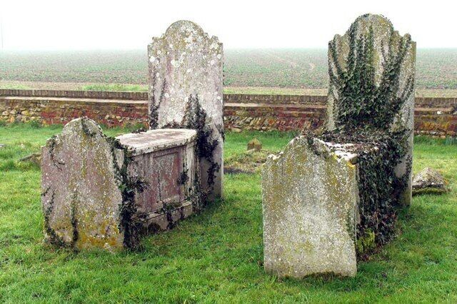 A graveyard with weathered headstones and a stone wall in the background.