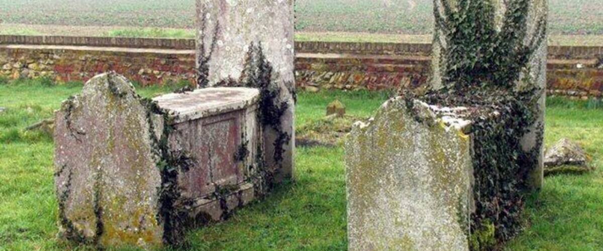 A graveyard with weathered headstones and a stone wall in the background.