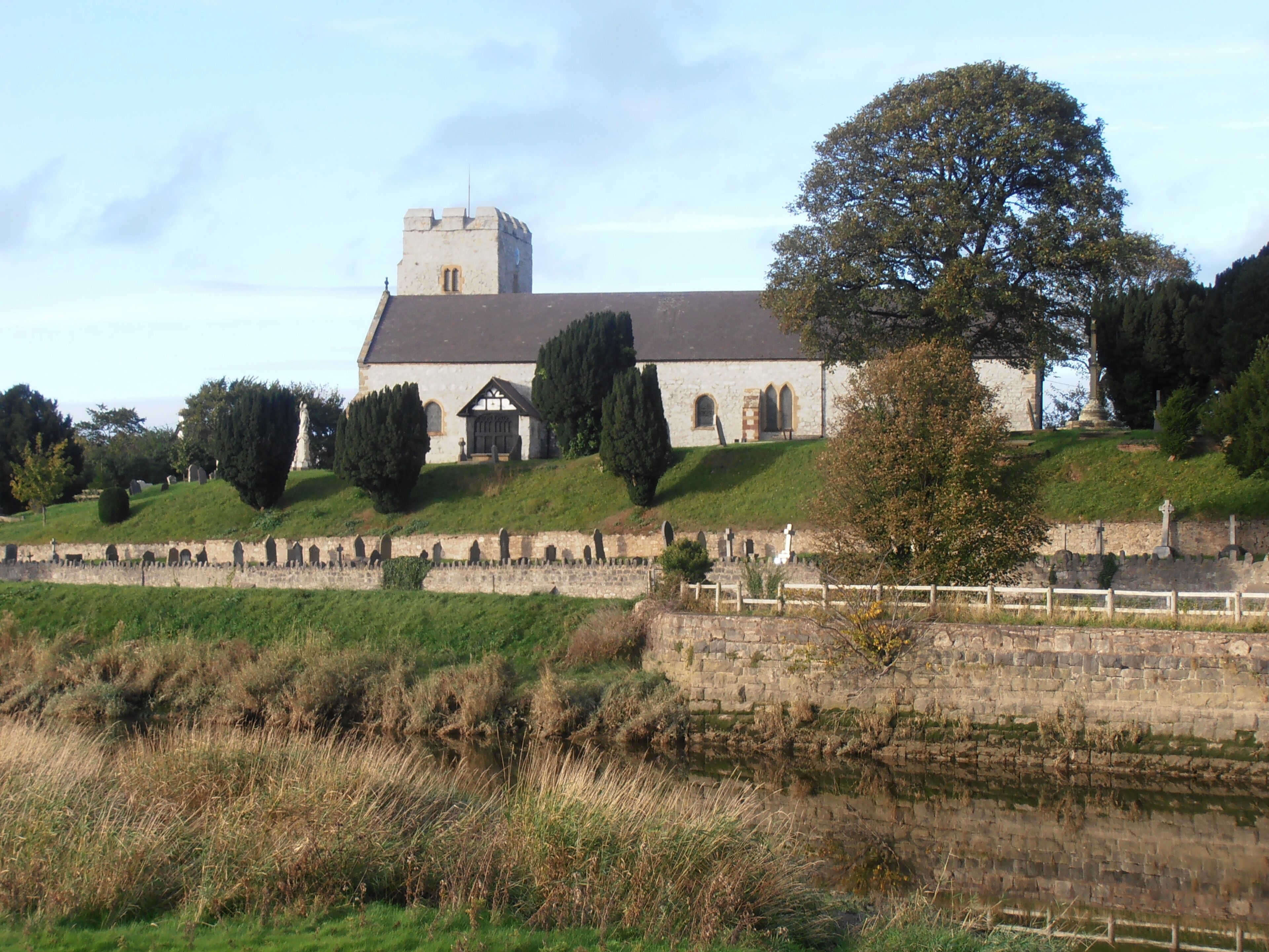 A church with a tower, surrounded by a cemetery and a stone wall.