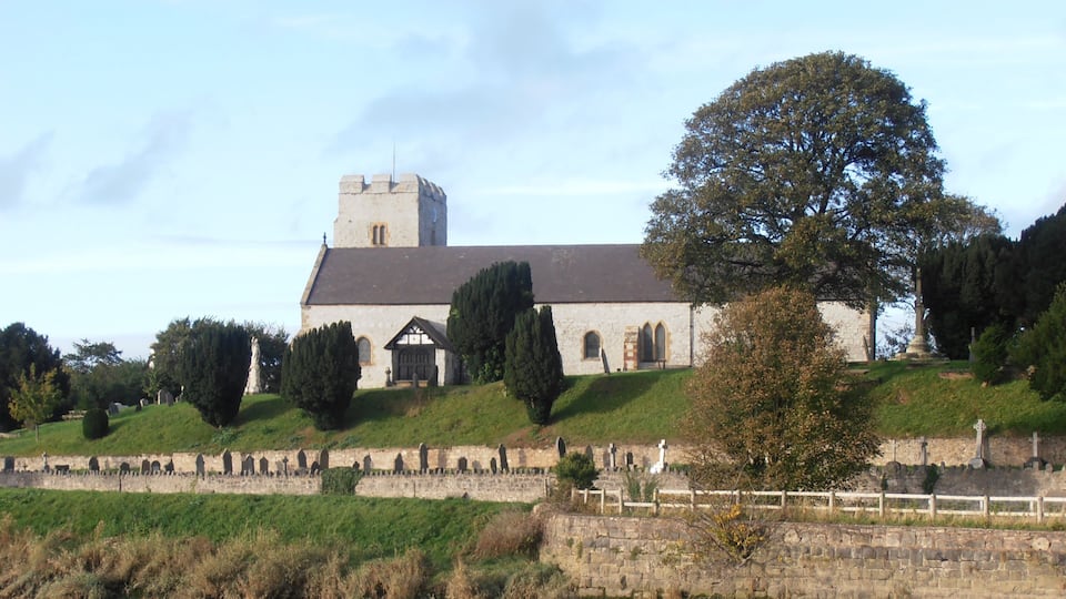 A church with a tower, surrounded by a cemetery and a stone wall.