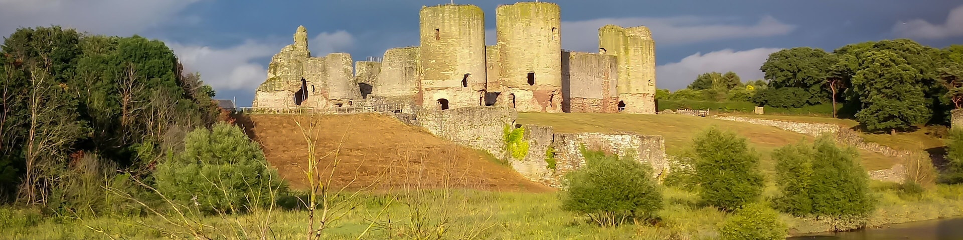 A historic stone castle with towers, surrounded by lush greenery and a calm river.