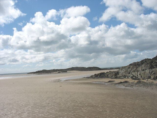 A wide sandy beach with rocky outcrops and a clear sky.