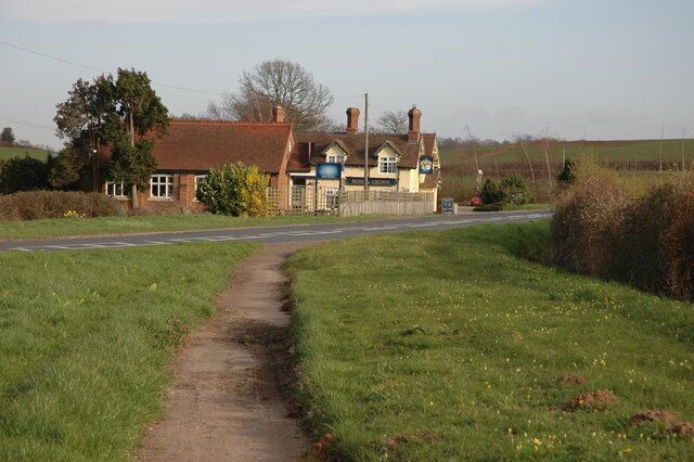 A rural road with a narrow path leading to a house with a blue sign.