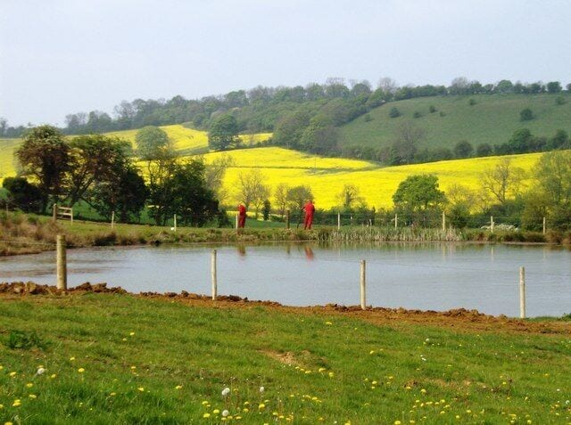 New pond, new fence The 1:25K map shows a spring here, but nothing this large. So this is a new pond, probably created for fishing use as part of the outdoor activity centre across the valley. These two men, in their corporate red overalls, are ensuring that they get the fence right.