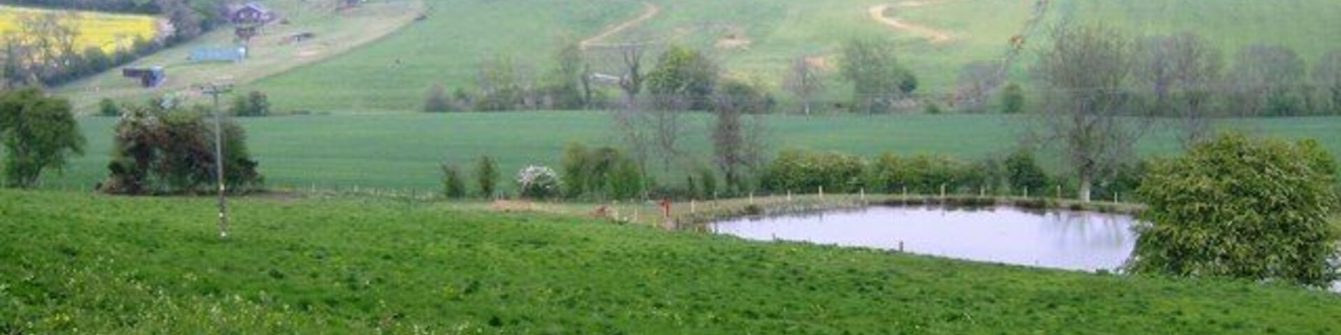 Outdoor activity centre This picture, taken from the western edge of the square, shows most of its northwestern quarter. A new pond in the foreground is built on the location of a spring. The land falls to a minor stream then rises to Camp Barn Farm on the left horizon. The area between is scored with tracks, all part of an outdoor activity centre where things like quad biking and scrambling are being practised. There was also the sound of airguns or clay pigeon shooting.