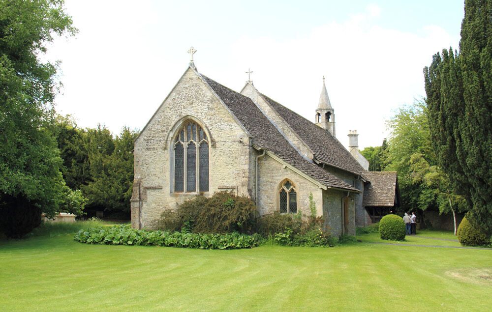 A stone church with a pointed roof and a steeple, surrounded by well-maintained grass and trees.