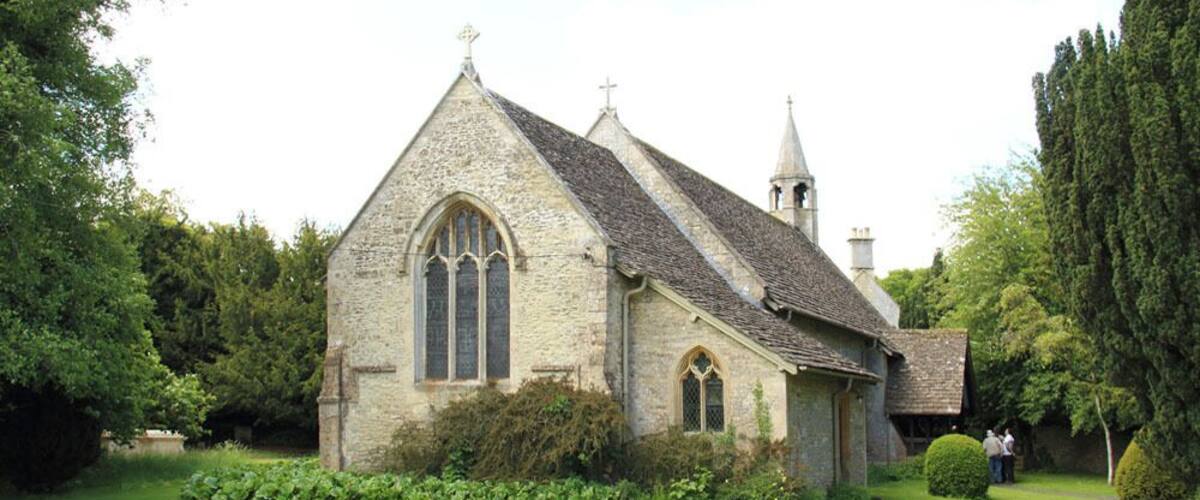 A stone church with a pointed roof and a steeple, surrounded by well-maintained grass and trees.