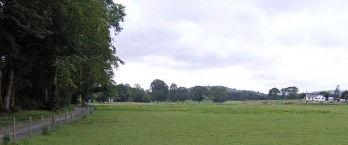 A grassy field with a fence, trees, and a distant building.