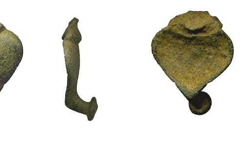 Cast copper alloy possible strap fitting. The body of the strap fitting is an inverted drop shape, which is wider than its length. The lower tip of the body has in an integral hook which forms a sub ‘L’ shape in profile. The terminal of the hook has a circular dome. The hook element, in section, is a pointed oval. The body of the object has a convex outer surface and the reverse is concave. The outer surface is decorated with two linear grooves forming a ‘/ \’ design. The upper edge of the body has an off-set integral curved platform which has a broken upper edge; therefore its original shape is undetermined. The reverse of this element of the fitting is obliquely angled. The surface of the fitting has frequent low-relief fitting with a dark green/grey patina. It is uncertain whether it is incomplete or a fragment of a larger object. It measures 28.26mm long, 28.95mm wide and 12.78mm thick across the hook element. It weighs 12.89g. The object is possibly a strap fitting; an element of a belt chain. Examples with a hook element terminating with a circular dome are described in Stead and Rigby (Stead, I and Rigby, V. 1999 Iron Age Antiquities From Champagne in the British Museum: The morel Collection British Museum Press), Nos. 1629 and 1901 which are dated to the late Iron Age. These examples were found in female graves in Champagne.