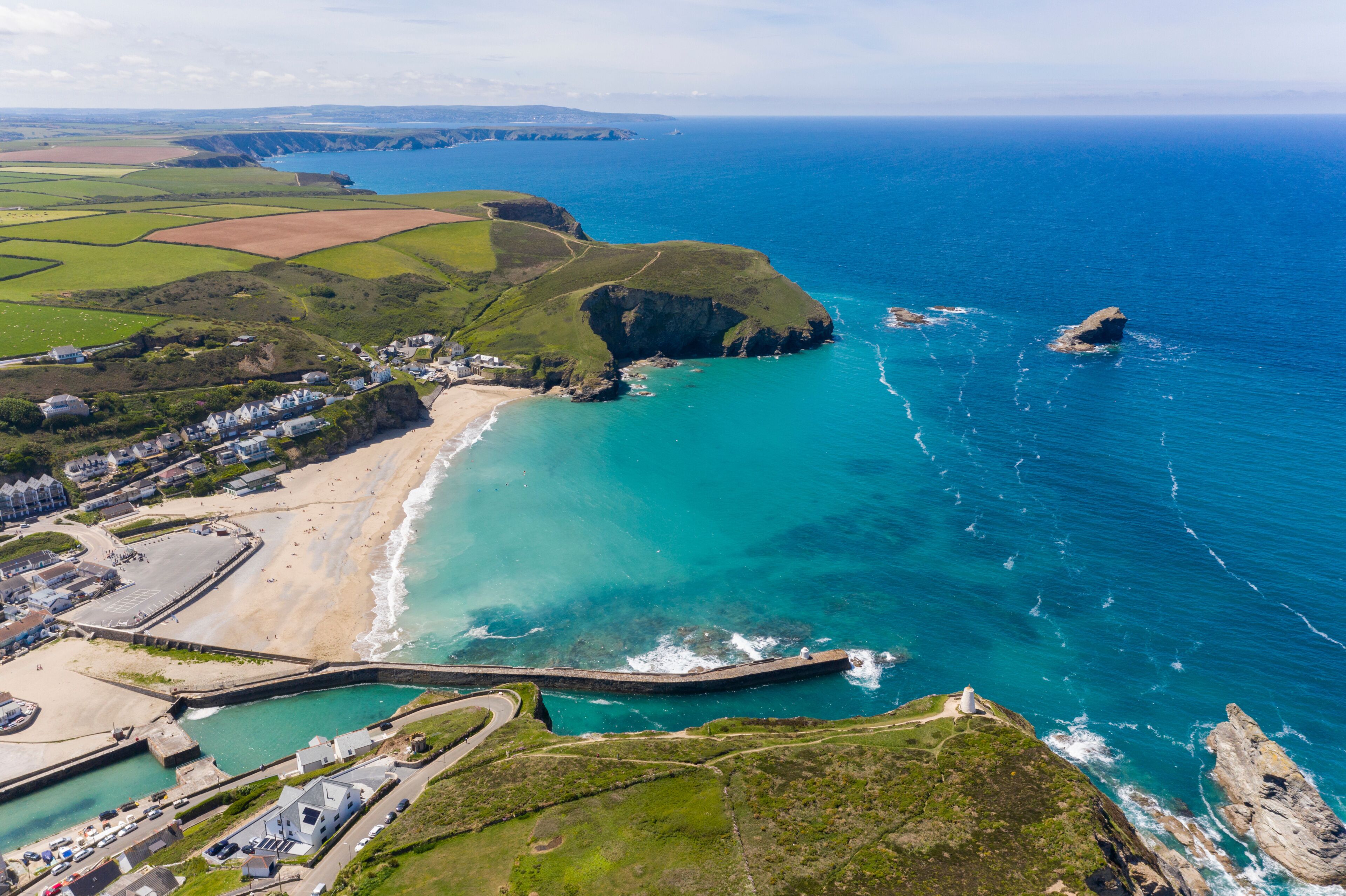 A coastal landscape with a beach, a lighthouse, and a winding road leading to a harbor.