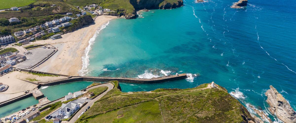 A coastal landscape with a beach, a lighthouse, and a winding road leading to a harbor.