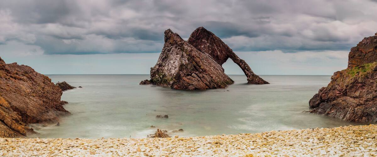 A rocky coastal landscape with a prominent rock formation in the center.