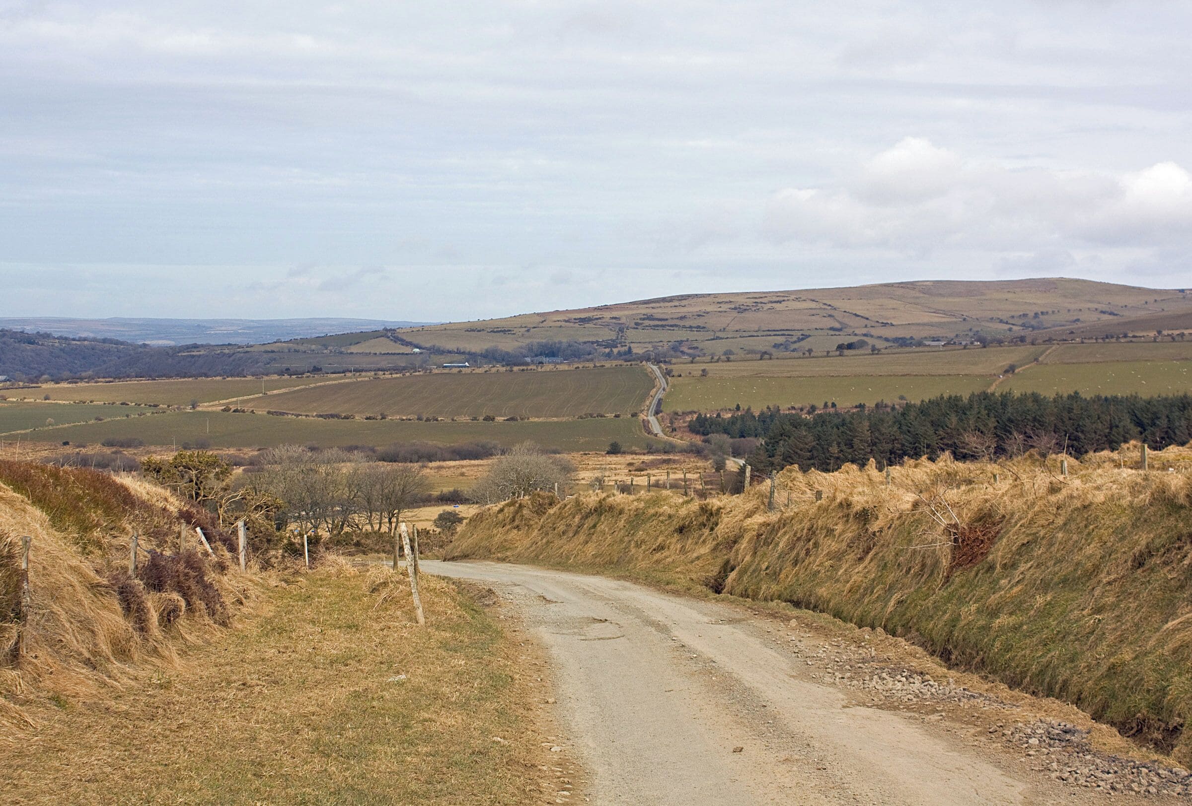 A rural road winding through a hilly landscape with fields and sparse vegetation.
