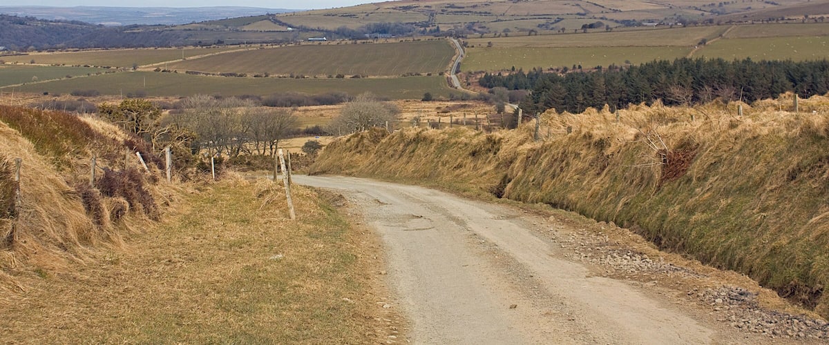 A rural road winding through a hilly landscape with fields and sparse vegetation.