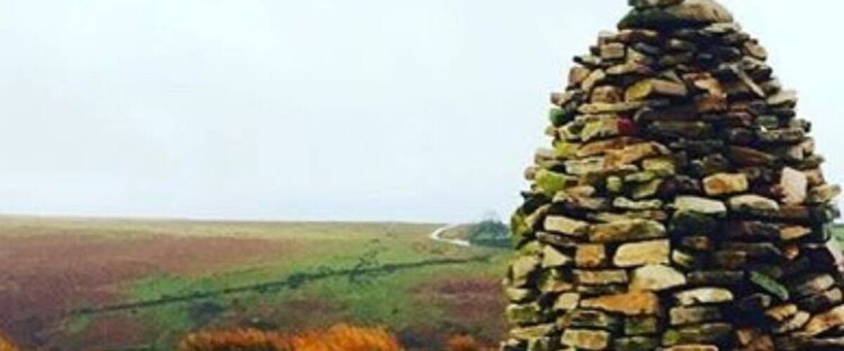 A stone cairn in a grassy field with rolling hills in the background.