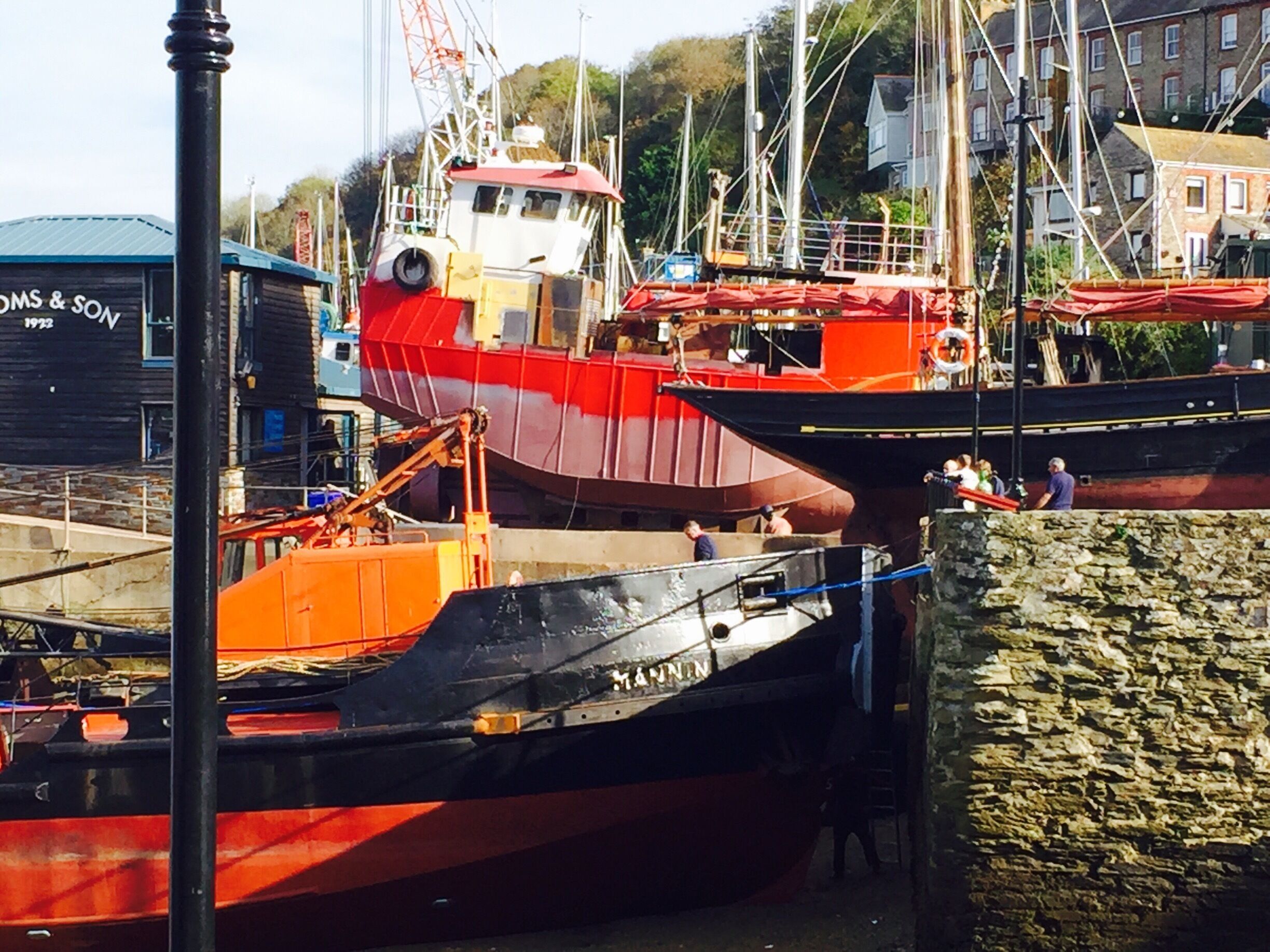 A dock with several boats, including a red and black ship named "MAMMUT" and a blue ship named "DOMS & SON."