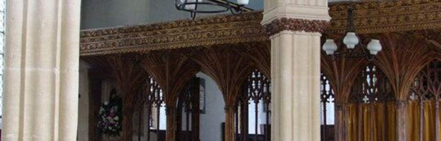 Interior de una iglesia con techos abovedados, bancos de madera y vidrieras.