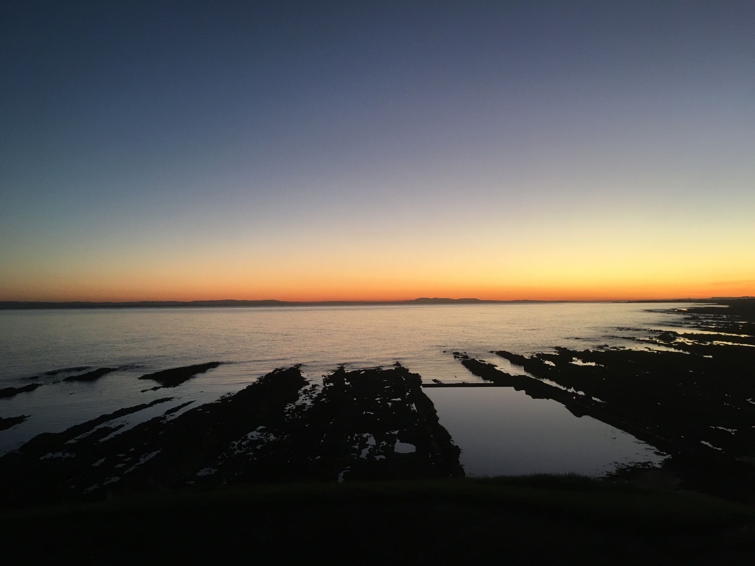 A sunset over a calm sea with rocky shores.