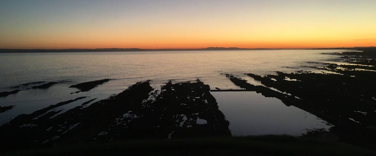 A sunset over a calm sea with rocky shores.