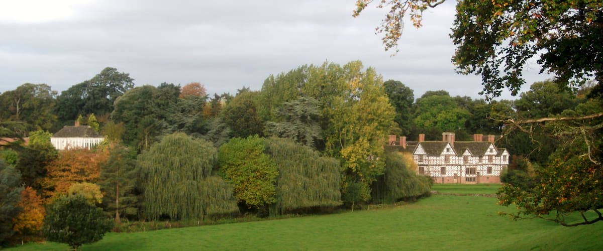 A large, white, Tudor-style house surrounded by lush greenery and trees.
