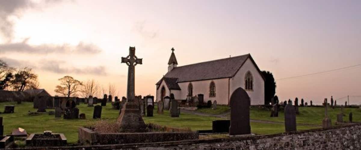 A church surrounded by a cemetery with headstones and a stone wall.