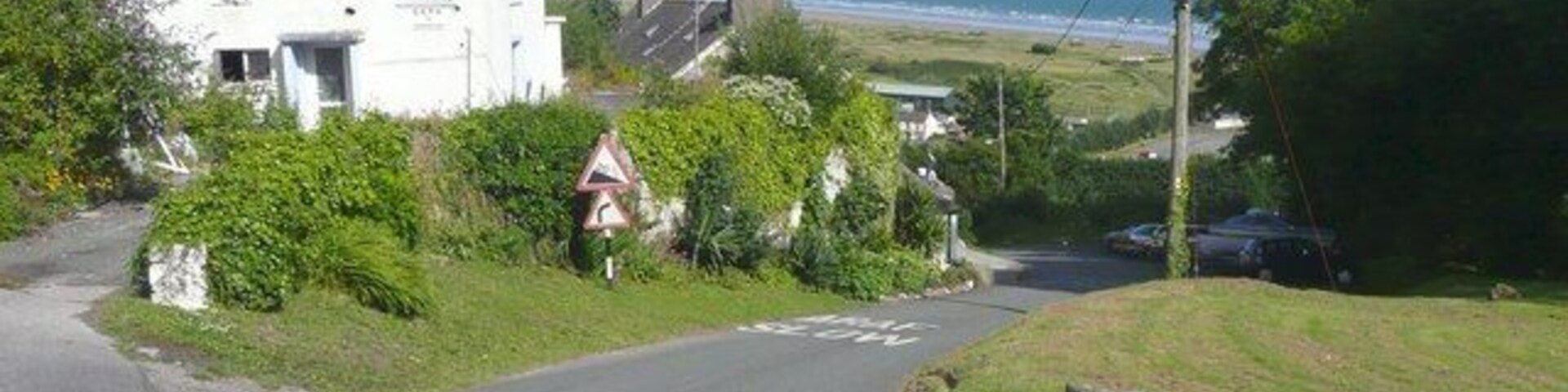 Un camino rural con una casa blanca, un cartel de advertencia y vistas al mar.