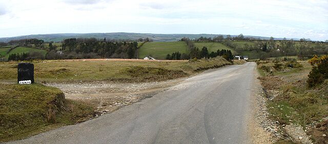 A rural road with grassy fields and hills in the background.