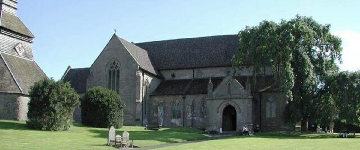 A church with a large lawn in front, a stone building, and a large tree.