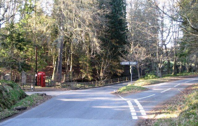 A rural road with a directional sign, a red telephone booth, and a forested area.